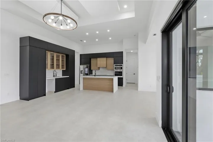 Kitchen with modern cabinets, light countertops, a center island with sink, a tray ceiling, and a high ceiling