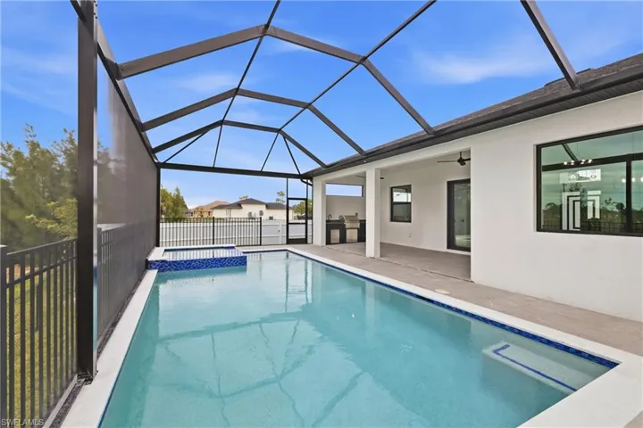 View of pool with a sunroom, a pool with connected hot tub, glass enclosure, a patio area, and an outdoor kitchen