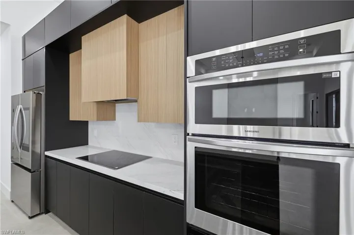 Kitchen featuring stainless steel appliances, modern cabinets, dark cabinetry, and light stone counters