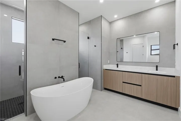 Bathroom featuring a shower stall, double vanity, a soaking tub, and tile walls
