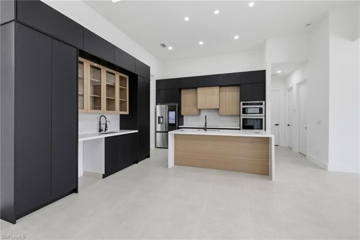 Kitchen featuring dark cabinetry, glass insert cabinets, a kitchen island with sink, modern cabinets, and appliances with stainless steel finishes