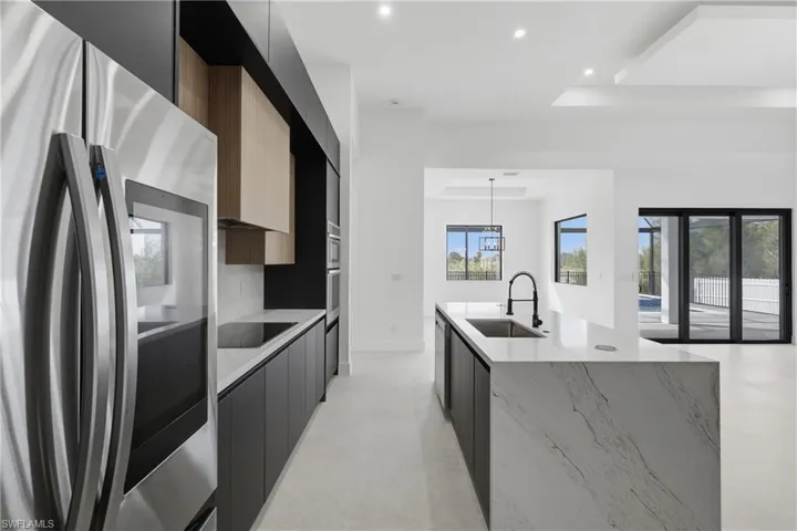 Kitchen with freestanding refrigerator, modern cabinets, light stone countertops, recessed lighting, and a center island with sink