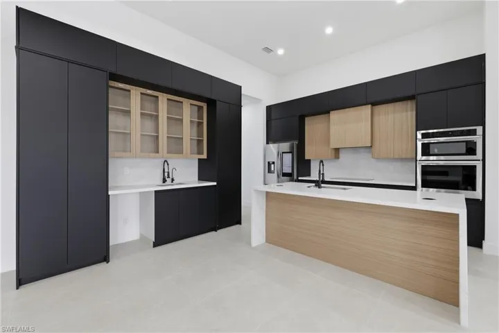Kitchen with dark cabinetry, modern cabinets, light brown cabinetry, a center island with sink, and light stone countertops