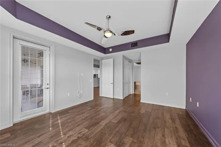 Unfurnished bedroom with a tray ceiling, wood finished floors, ensuite bath, and access to outside