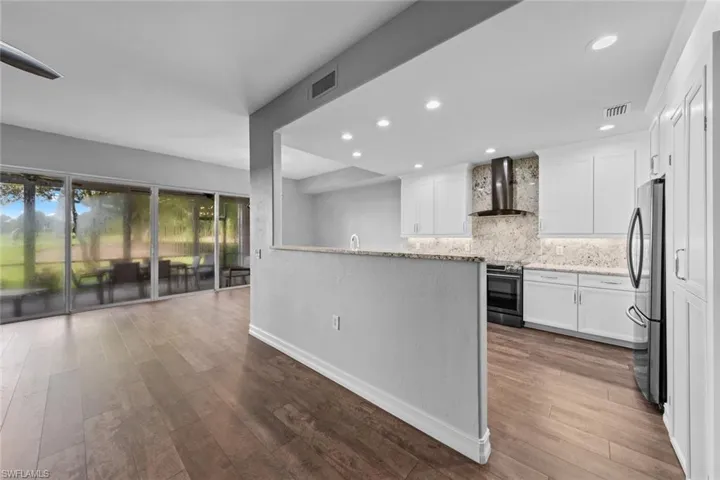 Kitchen with backsplash, recessed lighting, wall chimney exhaust hood, white cabinetry, and light stone counters