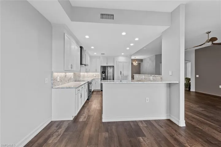 Kitchen with tasteful backsplash, dark wood-type flooring, a chandelier, light stone countertops, and recessed lighting