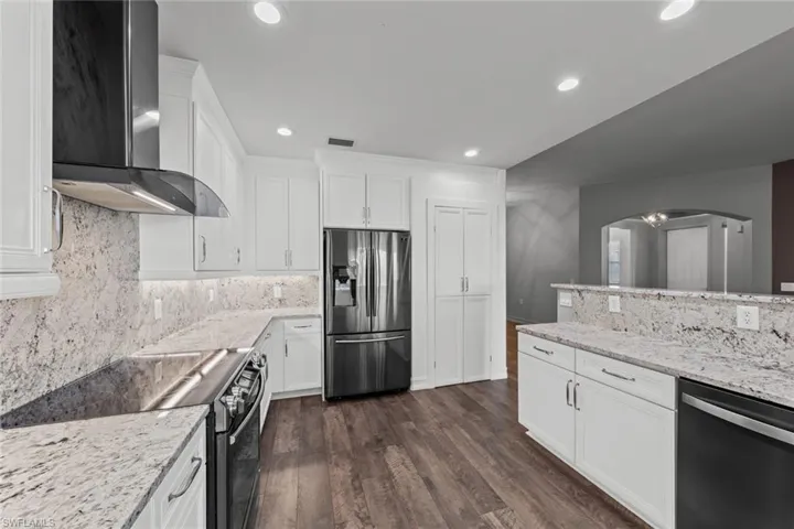 Kitchen with appliances with stainless steel finishes, backsplash, wall chimney range hood, dark wood-style flooring, and white cabinetry