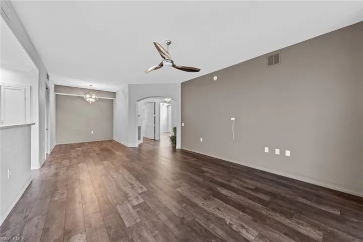 Unfurnished living room featuring arched walkways, ceiling fan, dark wood finished floors, and a chandelier