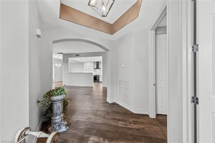 Hall with a tray ceiling, dark wood-style floors, a chandelier, and arched walkways
