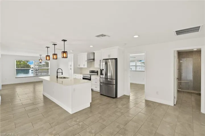Kitchen featuring appliances with stainless steel finishes, a sink, wall chimney range hood, light countertops, and white cabinets