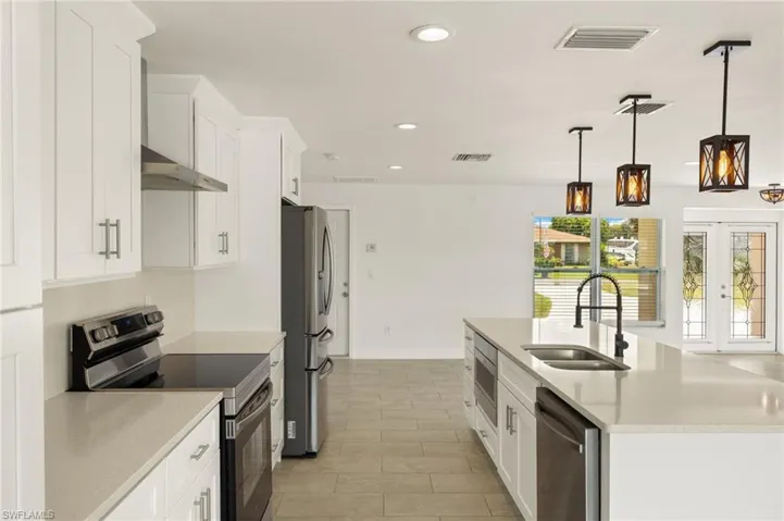 Kitchen featuring appliances with stainless steel finishes, a sink, under cabinet range hood, white cabinetry, and recessed lighting