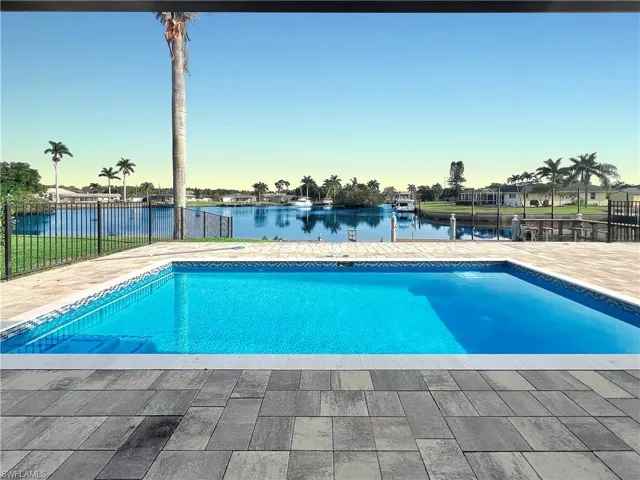Outdoor pool featuring a patio area, a water view, and fence