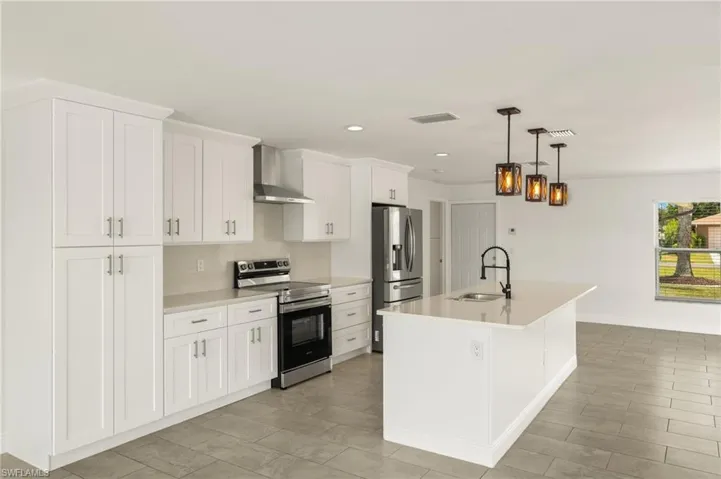 Kitchen with stainless steel appliances, wall chimney exhaust hood, a sink, light countertops, and a kitchen island with sink