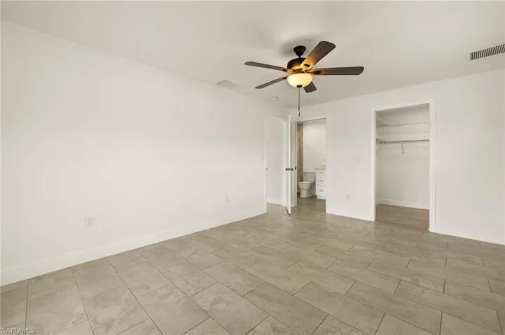 Unfurnished bedroom featuring a walk in closet, a closet, baseboards, and a ceiling fan