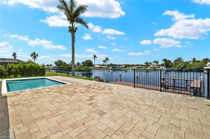 View of swimming pool with fence, a patio area, and a water view
