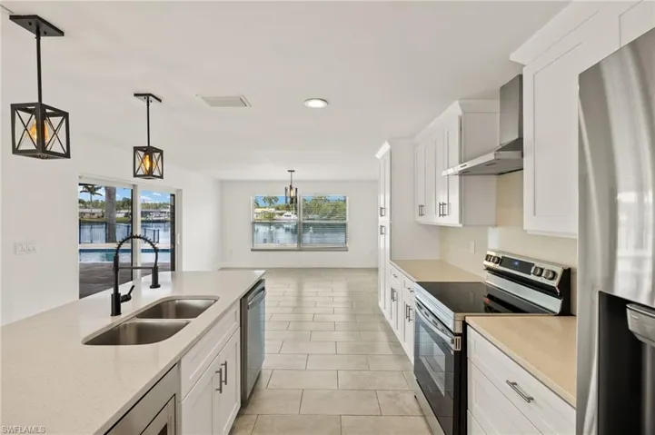 Kitchen with appliances with stainless steel finishes, a sink, wall chimney exhaust hood, white cabinetry, and decorative light fixtures