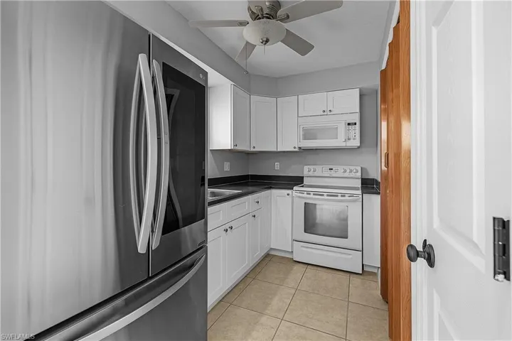 4014(L)  Kitchen featuring white appliances, new white shaker cabinetry, dark countertops, light tile patterned flooring, and ceiling fan