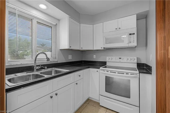4014(L)  Kitchen featuring white appliances, new white shaker cabinetry, dark countertops, light tile patterned floors, and recessed lighting