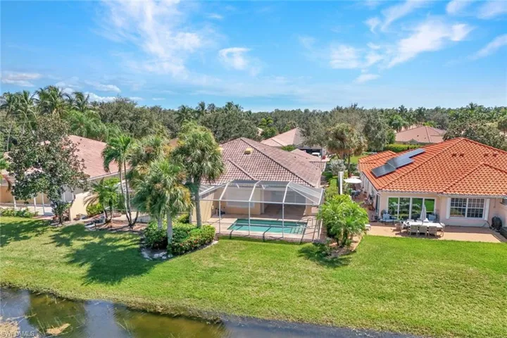 Expansive green lawn bordering a waterway, screened-in swimming pool, terracotta tile roof, solar panels, and a paved outdoor patio
