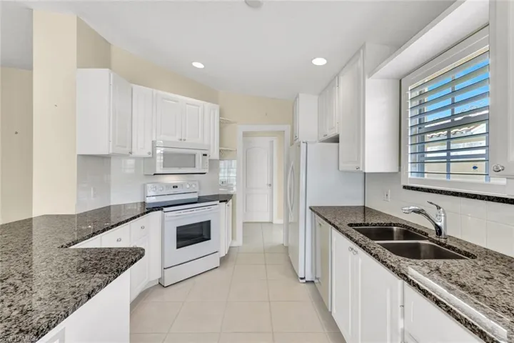 White cabinetry and appliances, granite countertops, tile flooring, and a double basin stainless steel sink