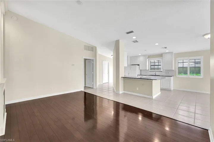 Vaulted ceilings, wood-finish flooring, white kitchen cabinetry, recessed lighting, and a kitchen island with a dark countertop