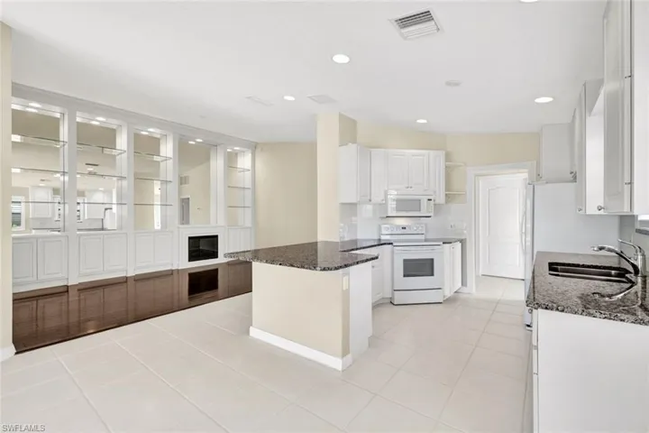 Built-in shelving with glass fronts and integrated lighting, white kitchen cabinetry, granite countertops, tile flooring, and a built-in electric fireplace