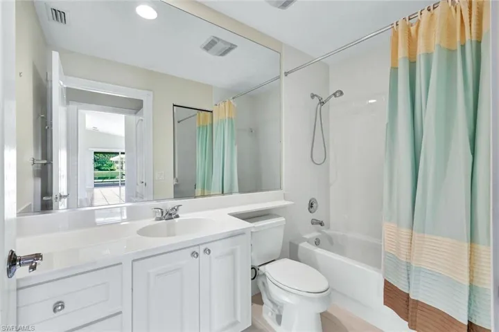 Bathroom featuring a white vanity with integrated sink, chrome faucet, wall-mounted mirror, and a combination shower/tub with a tiled surround
