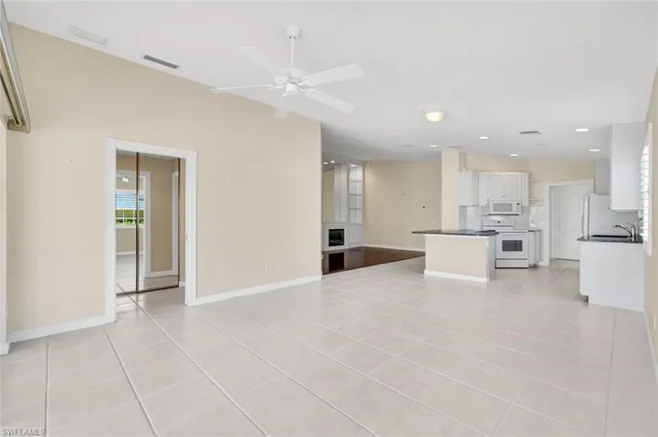 Open-concept living area with vaulted ceilings, large format tile flooring, and a ceiling fan