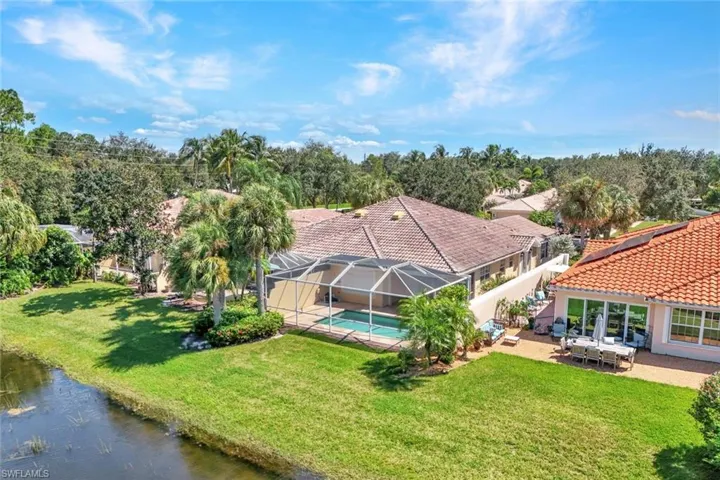 Tile roof residence with a screened-in pool enclosure, extensive green lawn, and mature palm trees