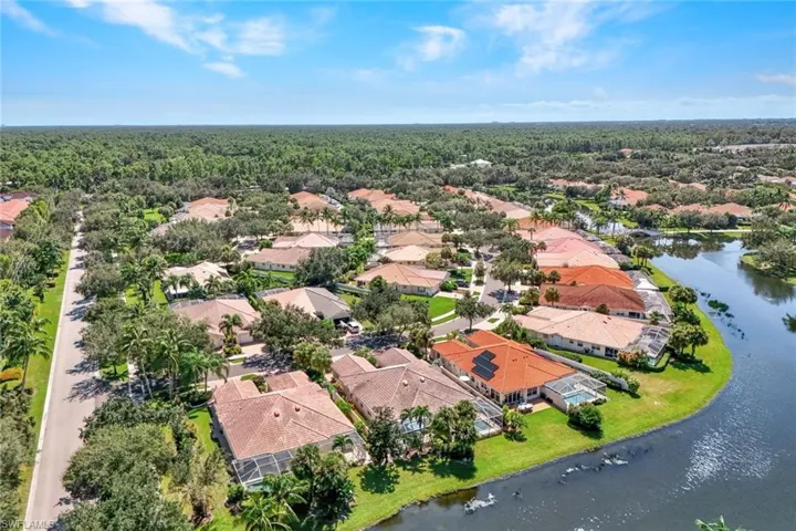 Aerial perspective featuring a residential community with tiled roofs, mature trees, and a water feature