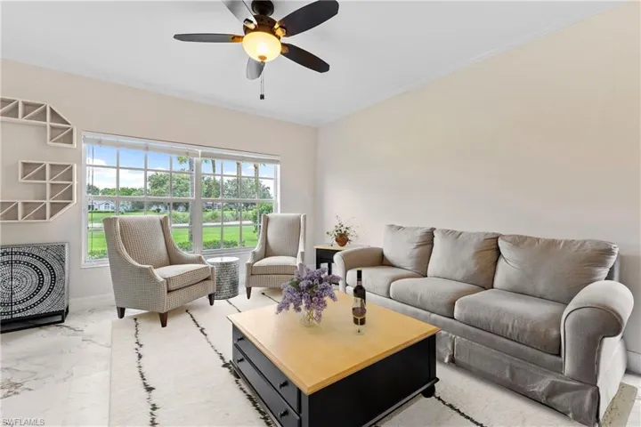 Living room featuring ornamental molding, a ceiling fan, and marble look tiles