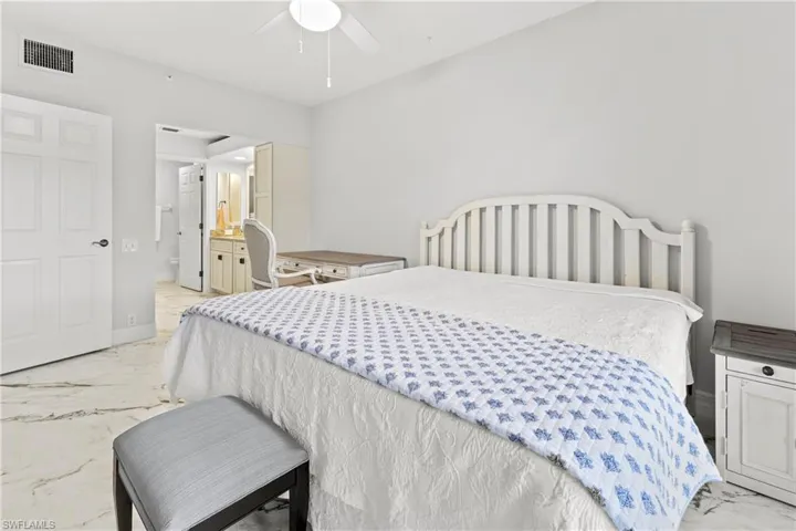 Bedroom featuring light marble finish floors, ensuite bathroom, and a ceiling fan