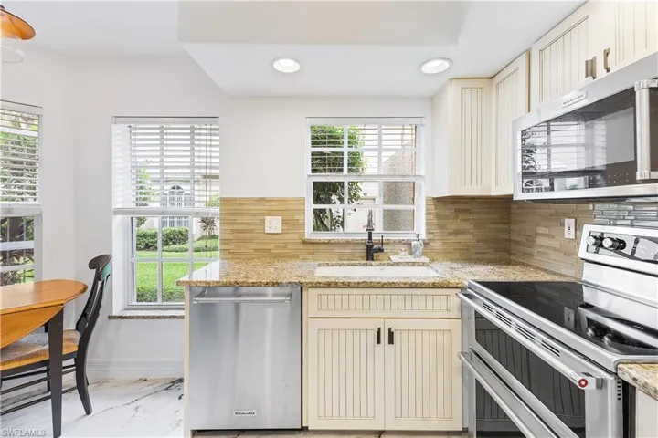 Kitchen featuring cream cabinetry, stainless steel appliances, decorative backsplash, recessed lighting, and light stone countertops