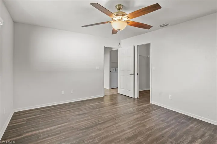 Unfurnished bedroom featuring dark wood-style floors, a spacious closet, ceiling fan, and washer / dryer