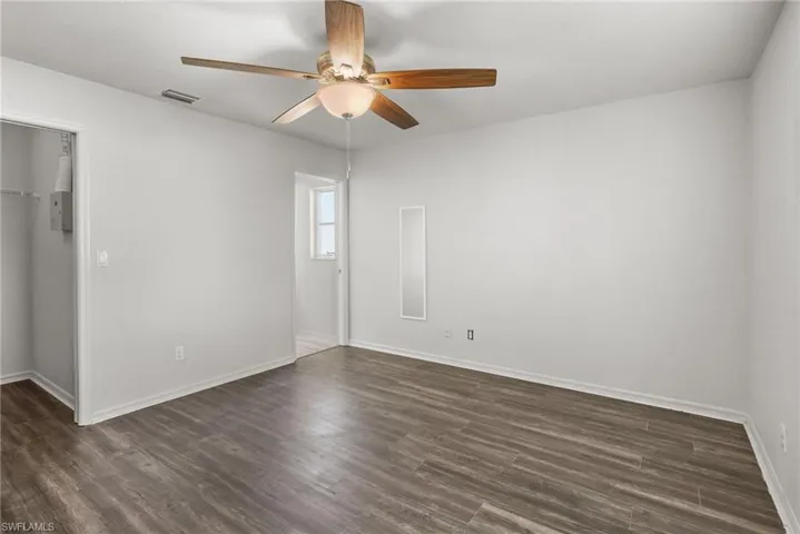 Unfurnished bedroom featuring a spacious closet, dark wood-style flooring, and ceiling fan