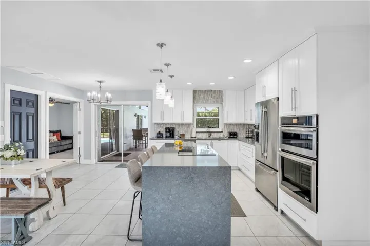 Beautifully updated kitchen with waterfall island, double oven, glass cooktop, glass backsplash, stainless steel appliances, white shaker cabinets, large sink overlooking the pool area. Easy access to outside space.