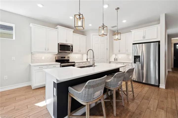 Kitchen with wood tiled floors, appliances with stainless steel finishes, white cabinets, a kitchen breakfast bar, and recessed lighting