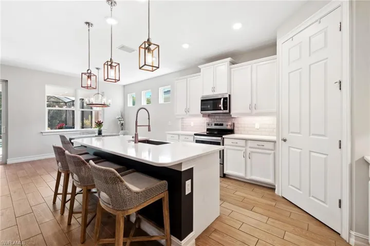 Kitchen with a kitchen island with sink, appliances with stainless steel finishes, a breakfast bar, decorative light fixtures, and wood tiled floors
