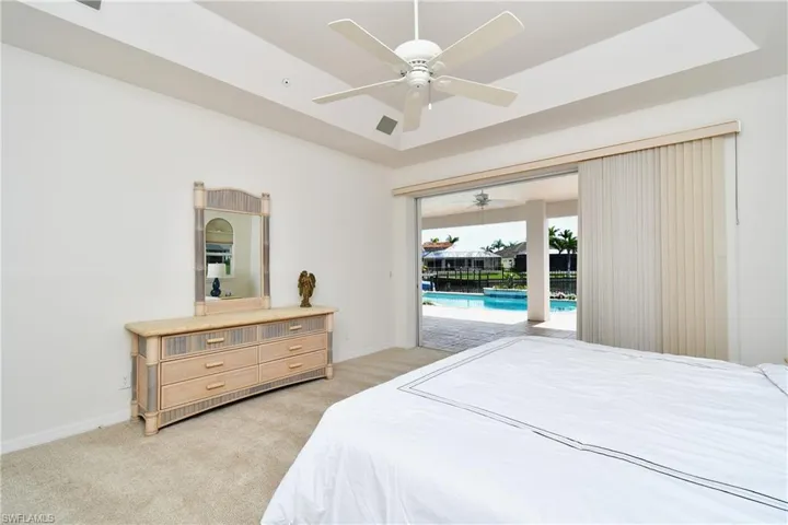 Carpeted bedroom featuring access to outside, ceiling fan, and a tray ceiling