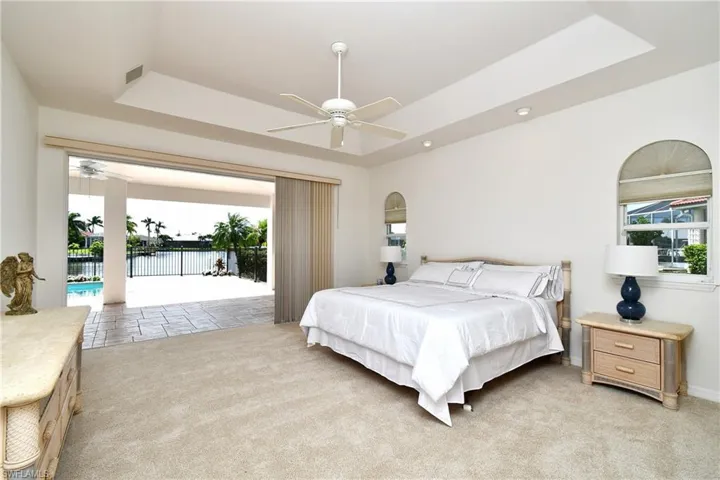Carpeted bedroom featuring ceiling fan, access to exterior, a raised ceiling, and a water view