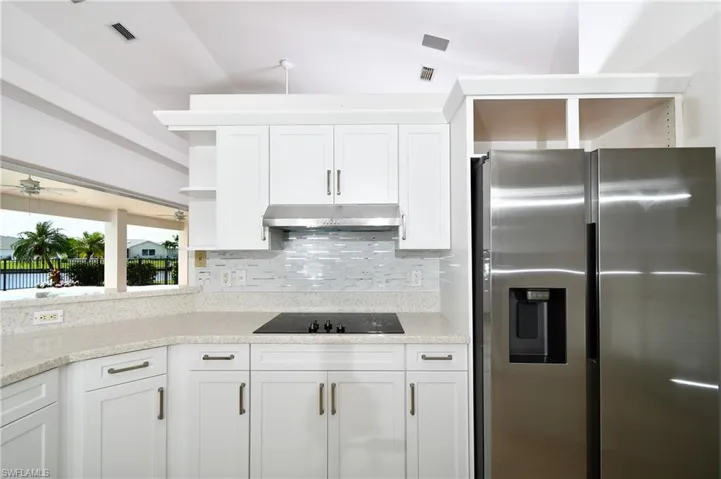 Kitchen with stainless steel fridge with ice dispenser, white cabinets, lofted ceiling, black electric cooktop, and ceiling fan