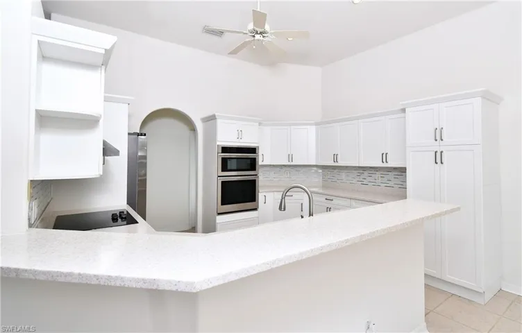 Kitchen with white cabinets, kitchen peninsula, light tile patterned flooring, and double oven