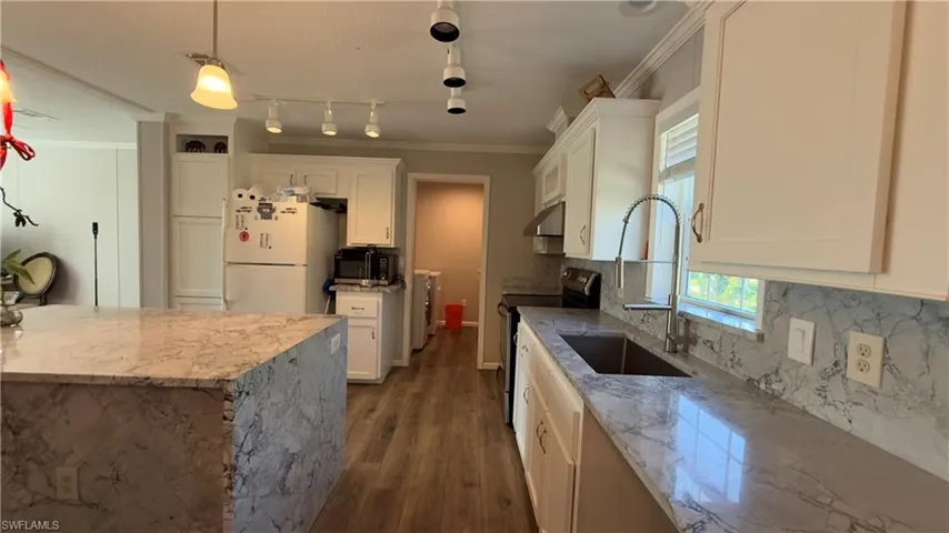 Kitchen featuring light stone counters, pendant lighting, range with electric stovetop, freestanding refrigerator, and ornamental molding