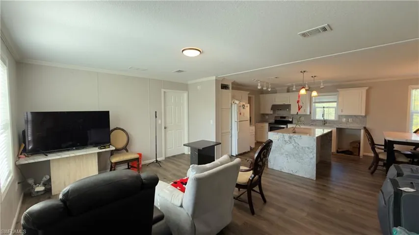 Living area with crown molding, dark wood-style flooring, track lighting, and a textured ceiling