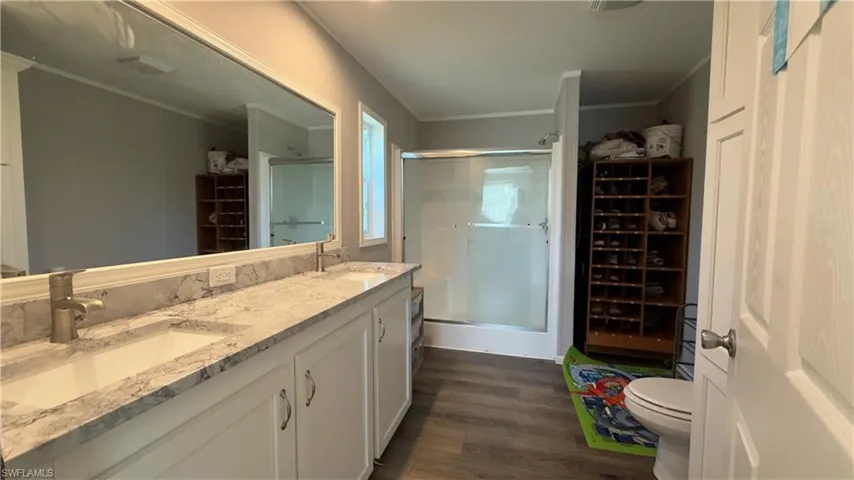 Bathroom with a spacious closet, a shower stall, double vanity, dark wood finished floors, and ornamental molding