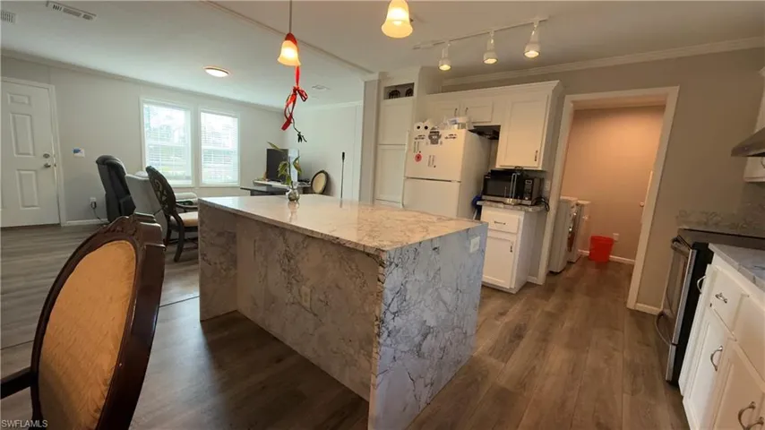 Kitchen with white cabinets, a kitchen island, crown molding, washing machine and dryer, and freestanding refrigerator