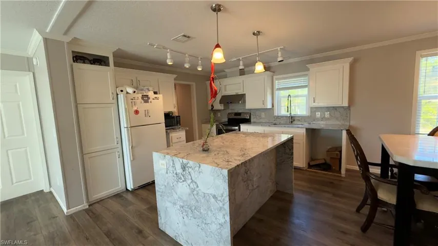 Kitchen featuring crown molding, freestanding refrigerator, decorative light fixtures, light stone countertops, and a kitchen island