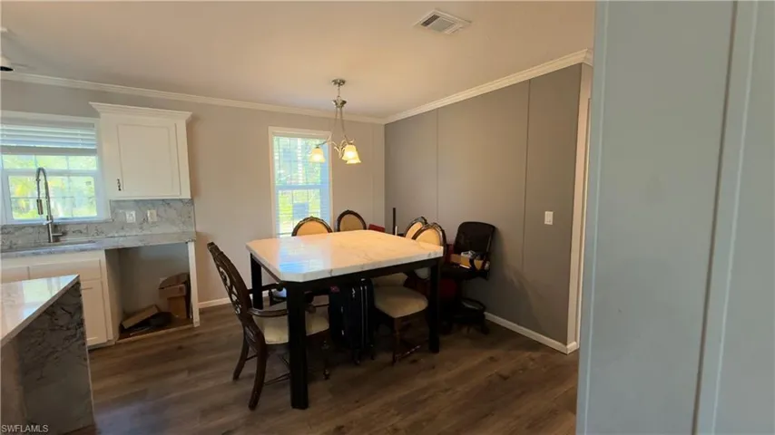 Dining room with ornamental molding, plenty of natural light, dark wood-type flooring, and a chandelier