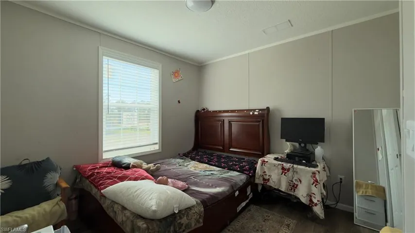 Bedroom with dark wood-type flooring, a textured ceiling, and crown molding