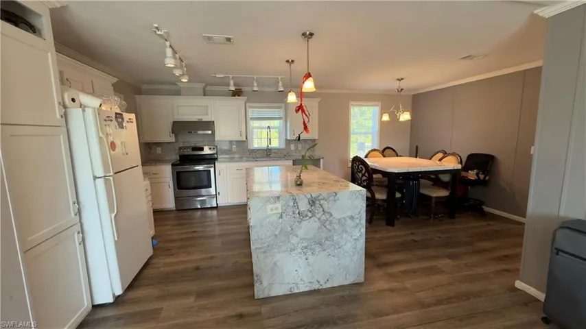 Kitchen with pendant lighting, ornamental molding, freestanding refrigerator, white cabinetry, and stainless steel range with electric cooktop